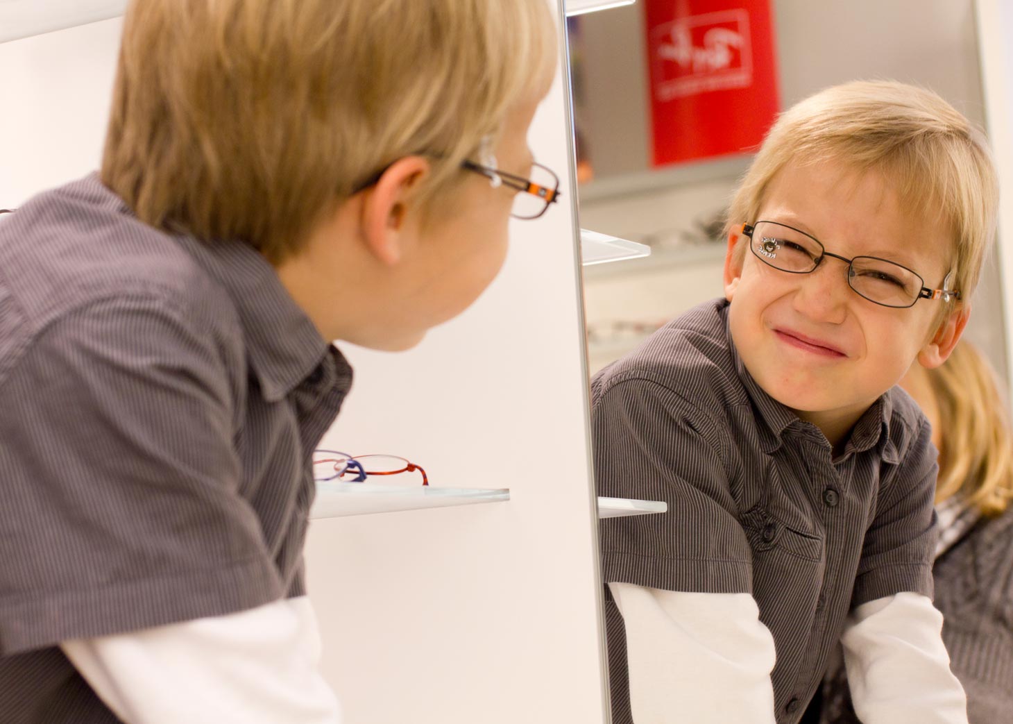 Junge mit Brille macht Grimasse beim Blick in den Spiegel